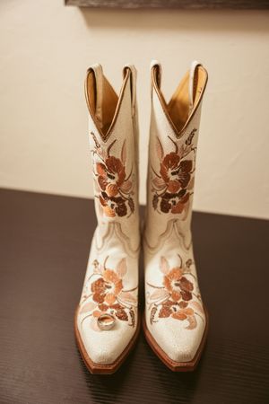 White leather cowboy boots with floral embroidery designs displayed on a dark wooden surface.
