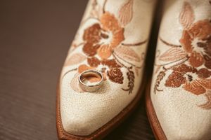 Vintage style floral embroidered leather shoes in beige and brown tones displayed on a dark wooden surface.