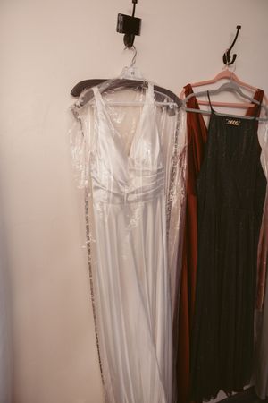 A white wedding dress and black garment hanging side by side on clothing hangers.