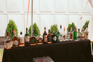 Long row of assorted liquor bottles displayed on a black-draped table at an outdoor event.