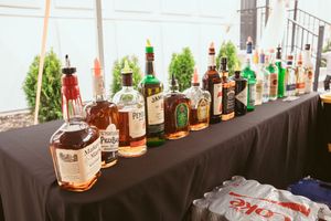 A collection of liquor bottles arranged on a black tablecloth at a wedding bar setup.