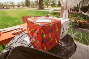 Festive red gift box with Christmas patterns sitting on a covered table outdoors.