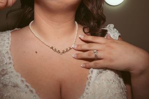 Close-up of bridal jewelry showing pearl necklace and diamond ring with white lace wedding dress detail.