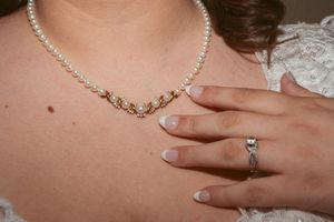 Close-up of a diamond necklace and engagement ring with French manicured nails.
