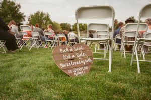 Wooden rustic wedding signs displayed on green grass with white chairs set up for an outdoor ceremony.