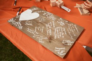 A wooden guest book board with white heart design and handwritten messages on an orange tablecloth.