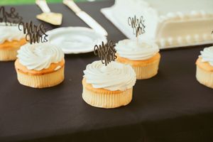 White frosted vanilla cupcakes with delicate chocolate accents displayed on a dark surface.