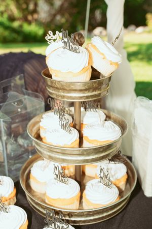 Tiered display stand of white frosted cupcakes with 'Mr & Mrs' decorative toppers.