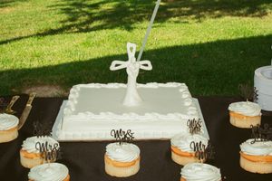 Row of tiered white wedding cakes decorated with flowers displayed on an outdoor table.