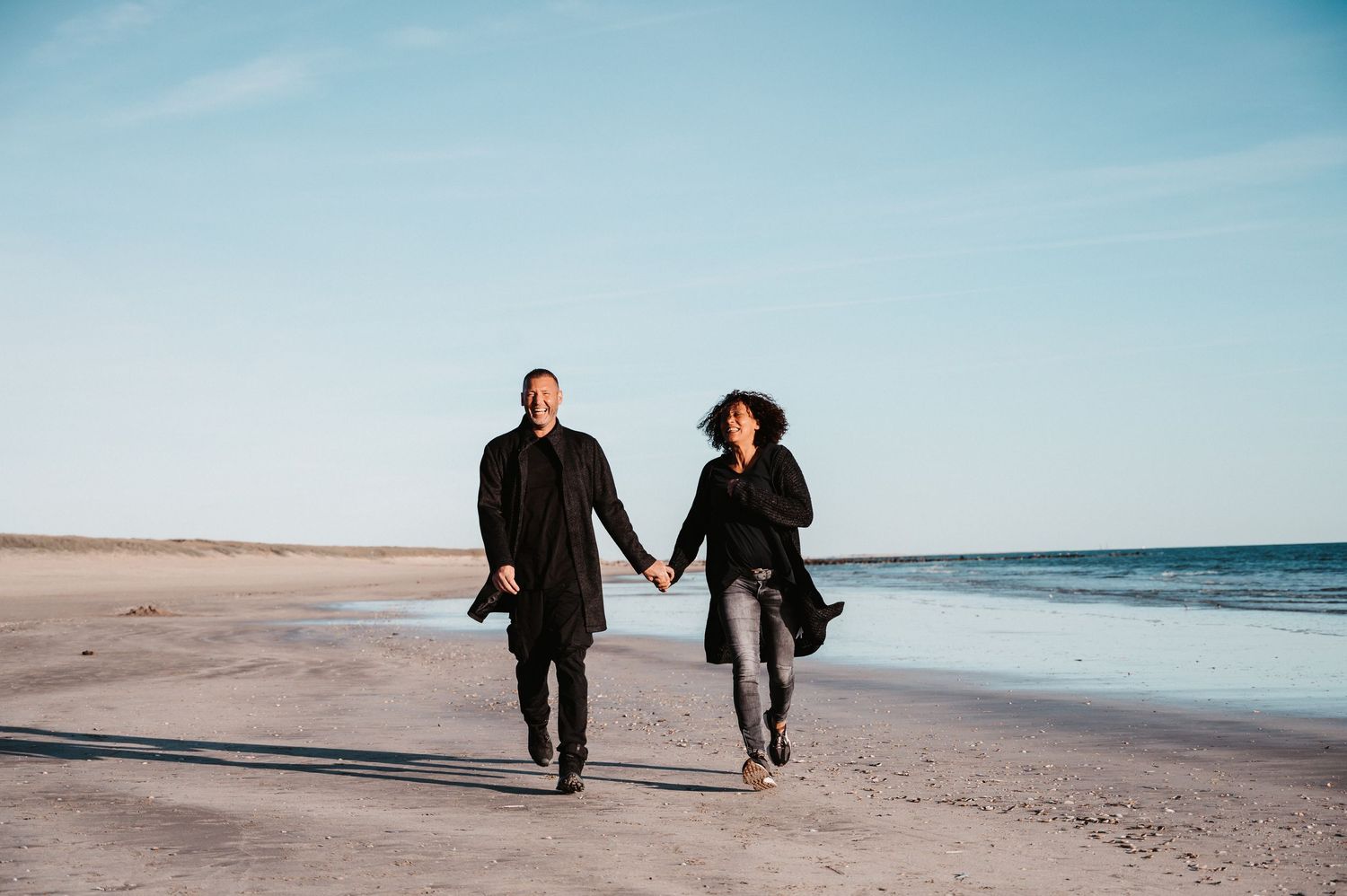 Ein Pärchen rennt , Hand in Hand , lachend am Strand in Dänemark auf den Fotografen zu.Es ist Sonnenuntergangslicht.
