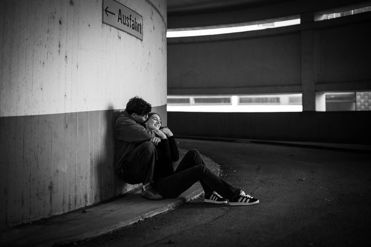 Schwarz-Weiß-Foto eines Paares in einem Parkhaus – beide lehnen an die Wand und sitzen auf dem Boden, urban, intim und stilvoll.