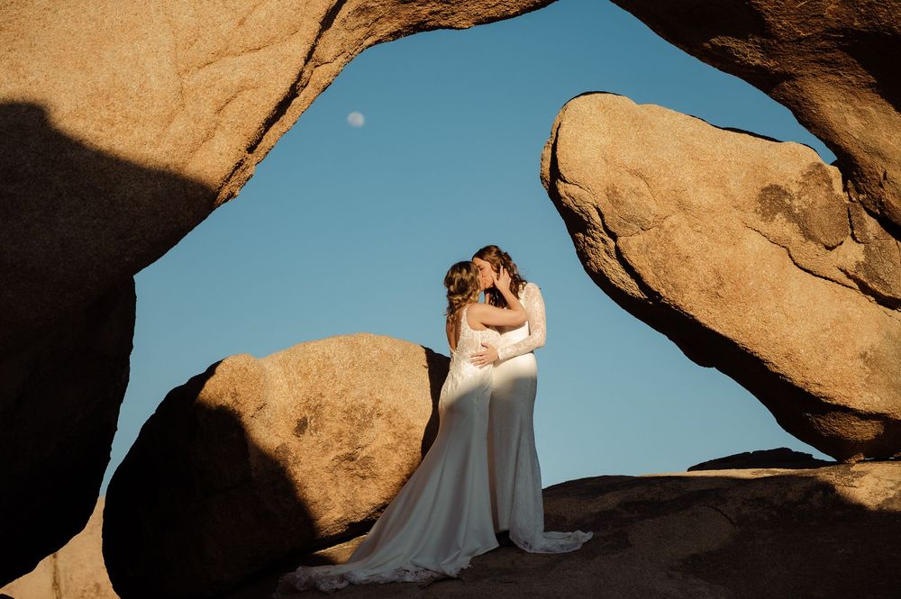brides kissing under moon at arch rock in Joshua Tree National Park