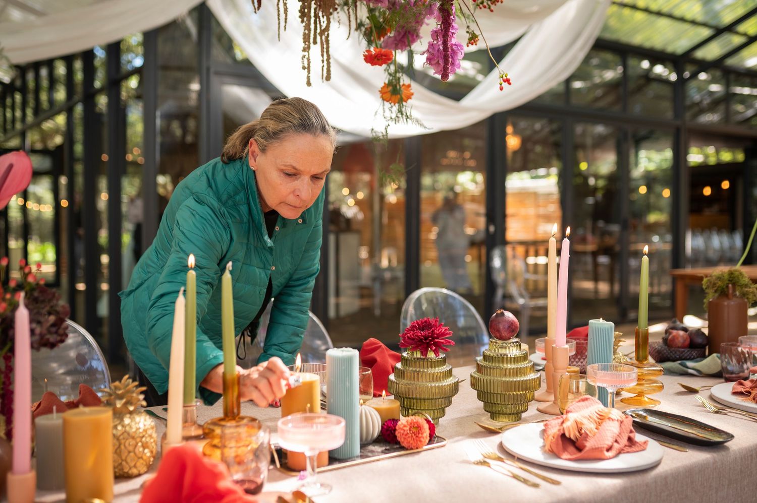 A festively decorated holiday dinner table with candles, ornaments and place settings being arranged in a restaurant setting.