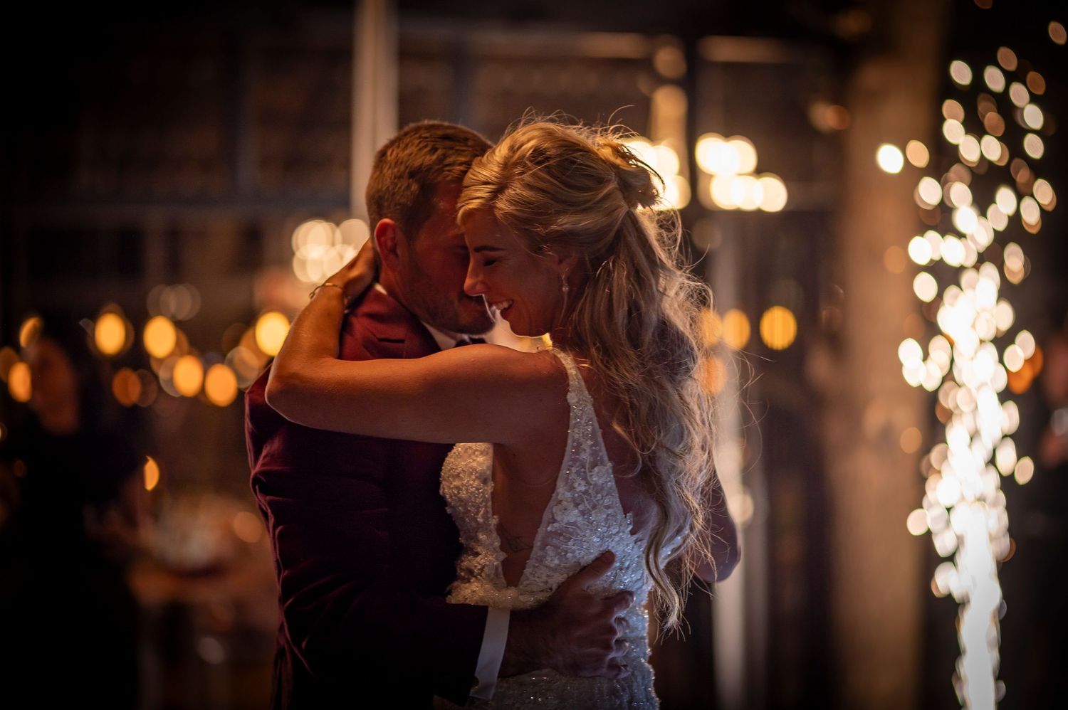 A couple shares their first dance as newlyweds with string lights and sparklers creating a romantic atmosphere.