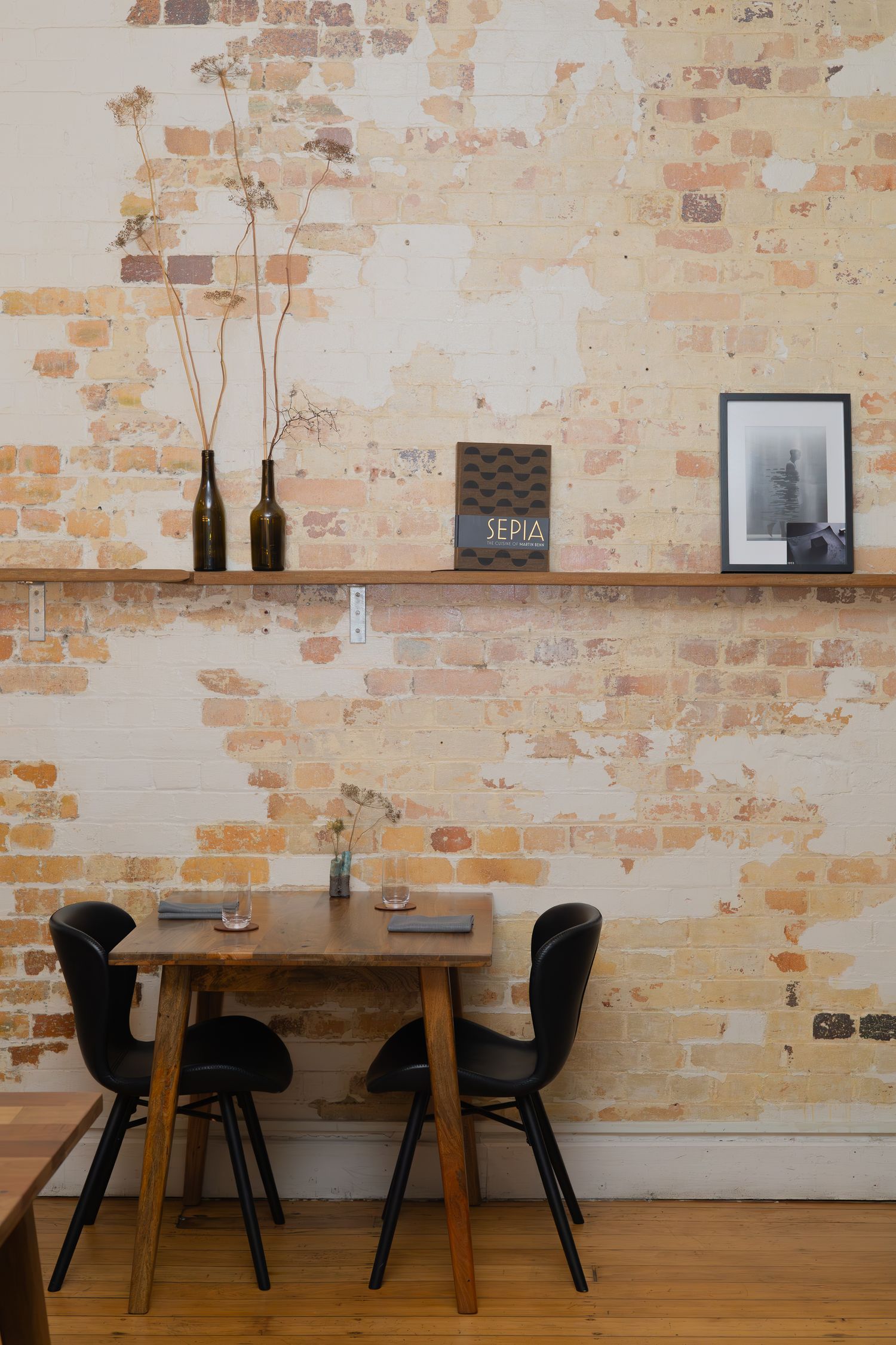 Modern restaurant interior with exposed brick walls, sleek wooden tables, and black chairs creating a minimalist ambiance.