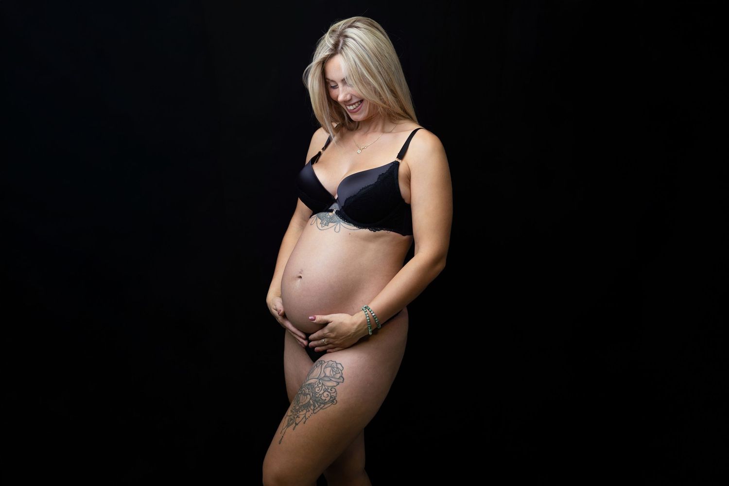 Artistic maternity photos in black lingerie against dark background.
