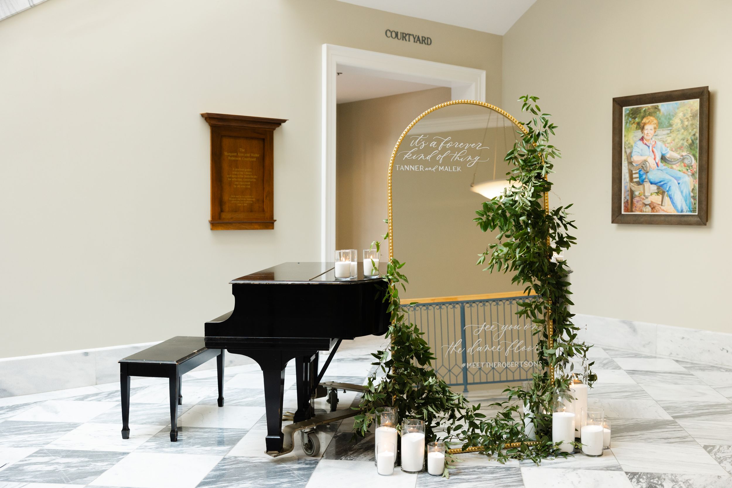 Elegant black grand piano with decorative greenery and lanterns by an arched doorway in a white marble hallway.