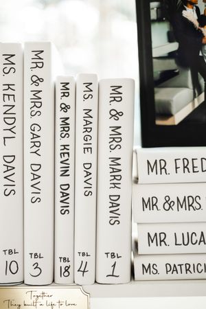 Wedding table seating books in white with black text showing Mr and Mrs names arranged on shelf with table numbers.