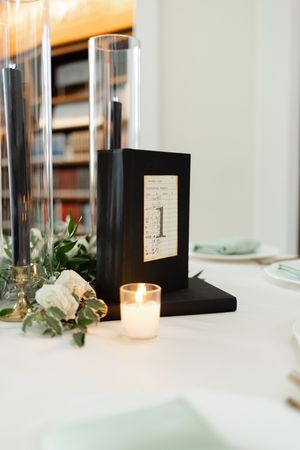 Black table number holder with candle and white floral decor on an elegant table setting.