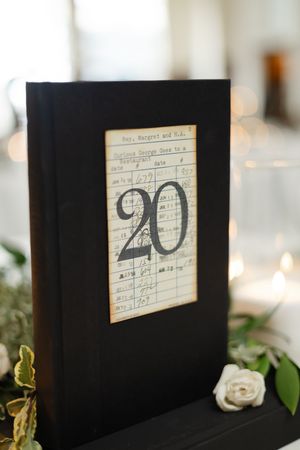 Close-up view of handwritten vintage index cards for table numbers in black frames with white roses as decor.