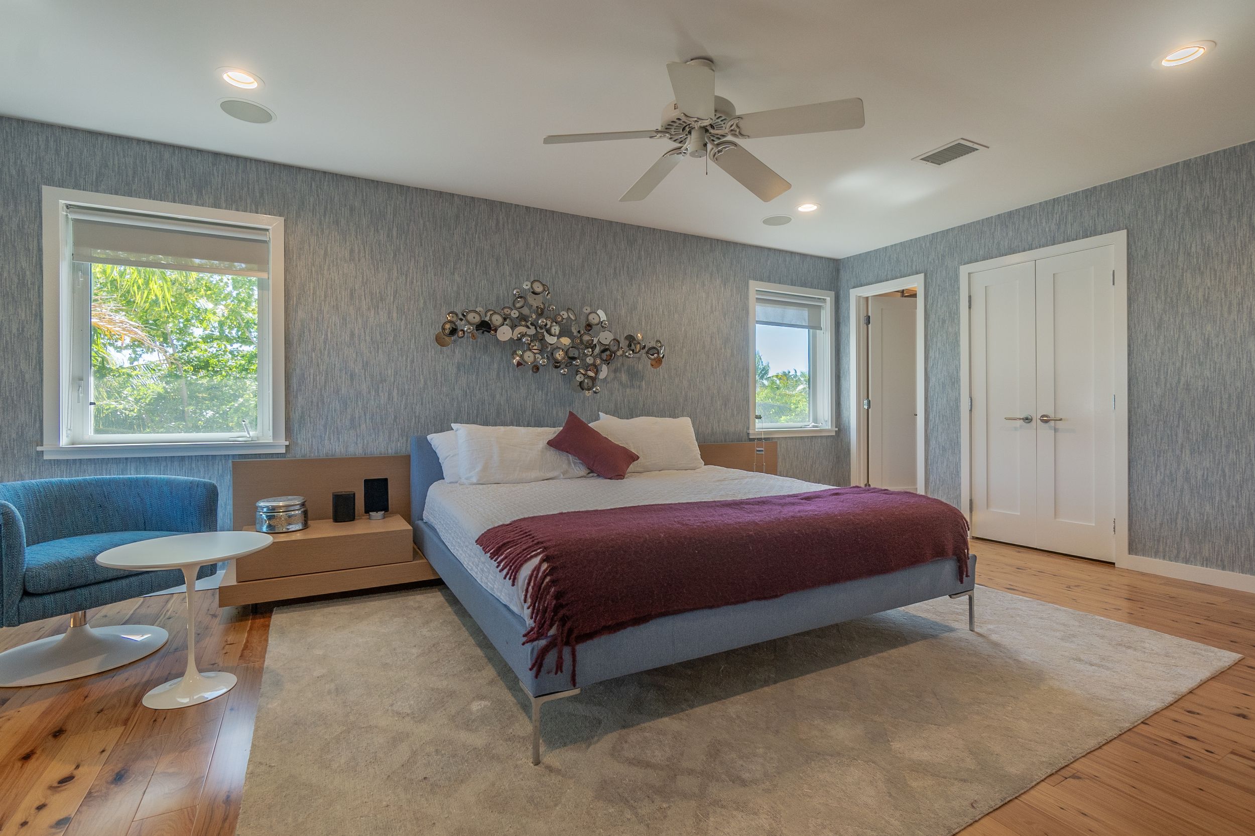 Spacious bedroom interior with gray wallpaper, ceiling fan, and large windows.