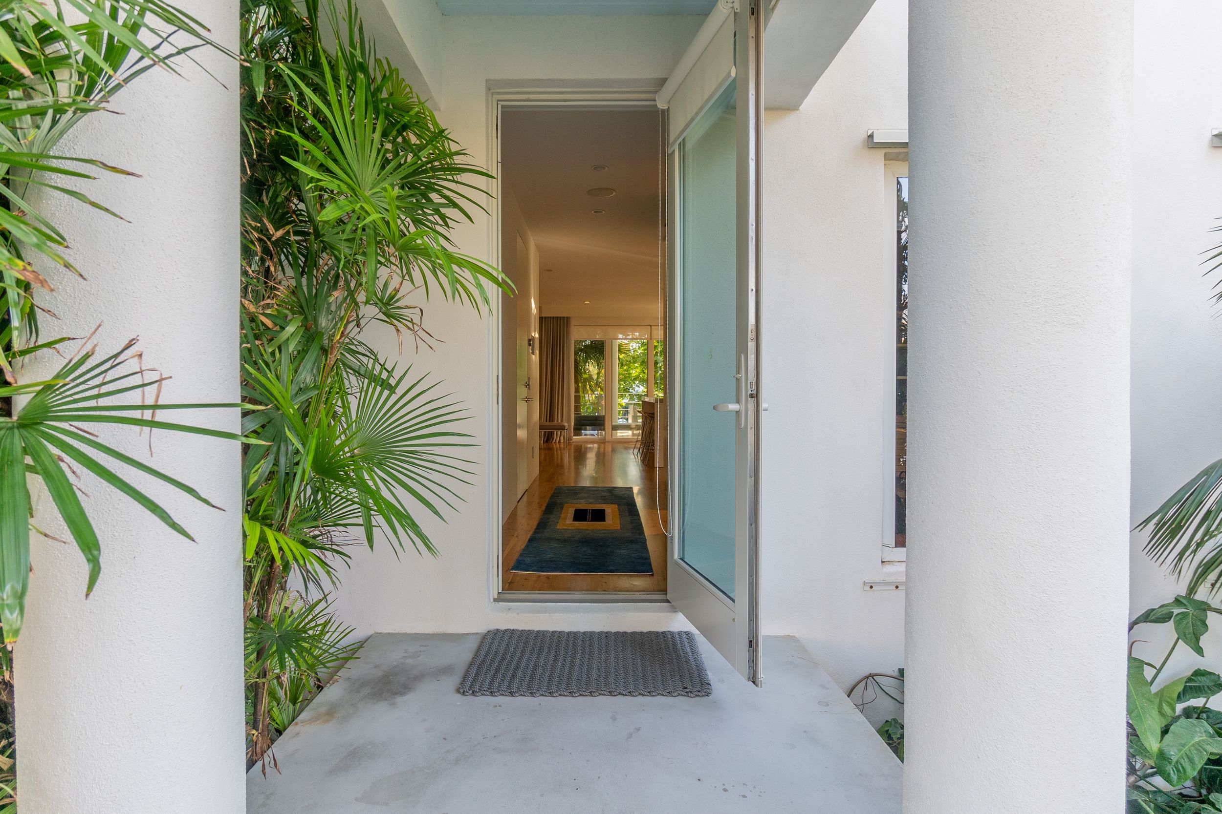Long hallway entrance with glass door, white walls and tropical landscaping.