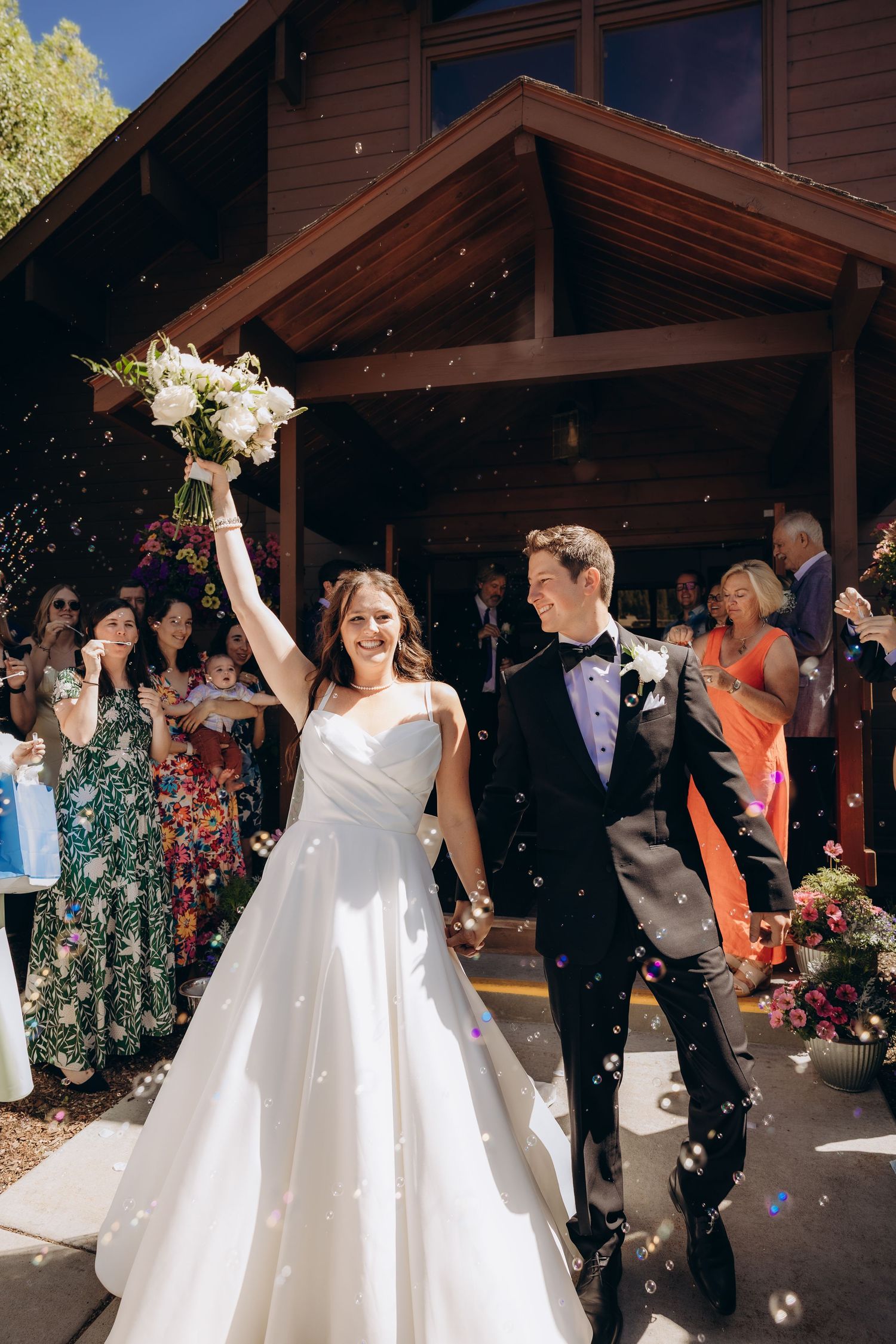 A wedding couple exits their venue while guests toss confetti and flower petals during a joyful celebration.