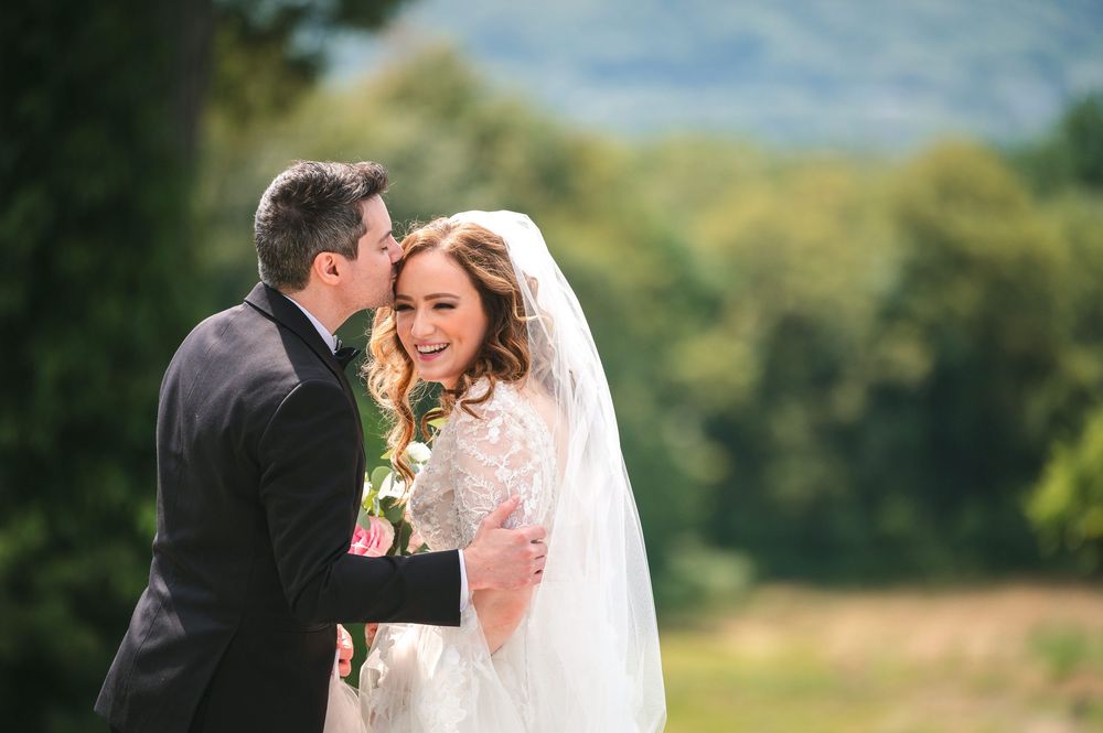 Couple shares romantic kisses during wedding portraits in lush outdoor setting with golden sunlight.