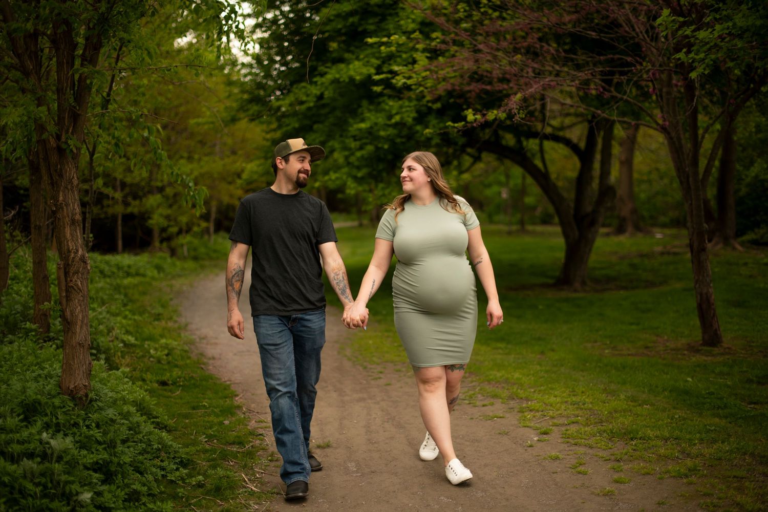 Happy couple walks together on a tree-lined path during golden hour photography session.
