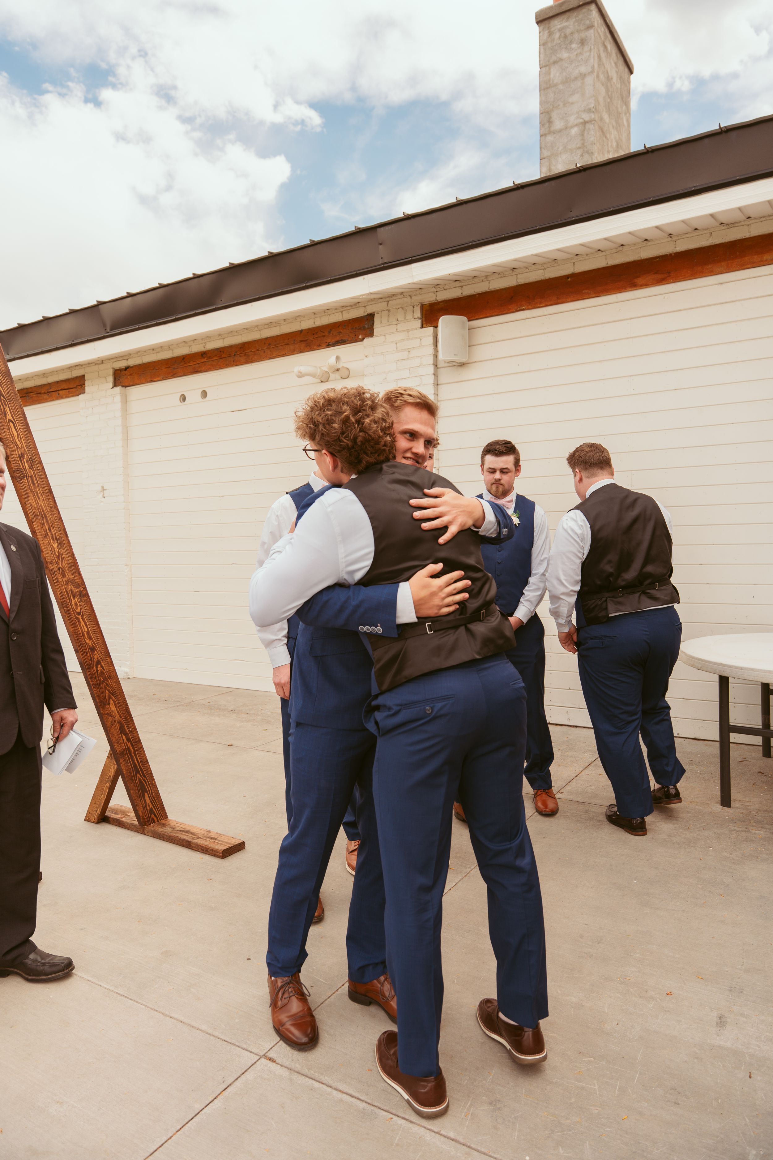A group of groomsmen in navy suits hunched over in a playful bowling motion outdoors.