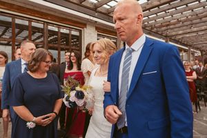 Guests in formal attire mingle and socialize at an indoor reception venue with exposed brick walls and wood beams.