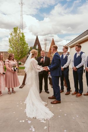 Wedding party in navy suits and blush pink dresses poses in a line outside on a sunny day with church spires in background.