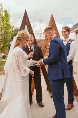 An intimate wedding ceremony takes place under a wooden triangular arch with geometric details.