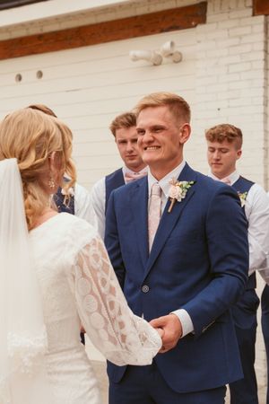 Wedding ceremony participants share a joyful moment outside against a white brick wall.