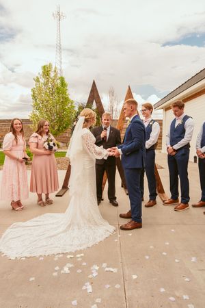 A wedding party lineup outdoors with bridesmaids in blush dresses and a bride in a flowing white gown with long train.