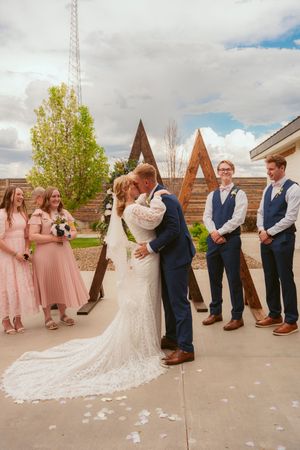 Wedding party in navy suits and pink dresses poses outdoors against rustic backdrop during ceremony sequence.