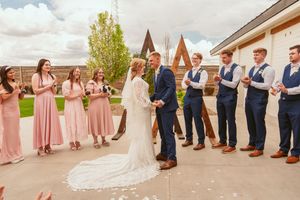 Wedding party stands in line with bridesmaids in blush pink dresses and groomsmen in navy suits at outdoor ceremony.