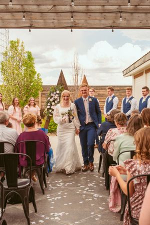 Wedding ceremony guests seated on dark chairs with white petals scattered along wooden deck venue.
