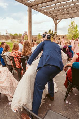 Wedding guests mingle under a wooden pergola during an outdoor reception celebration.