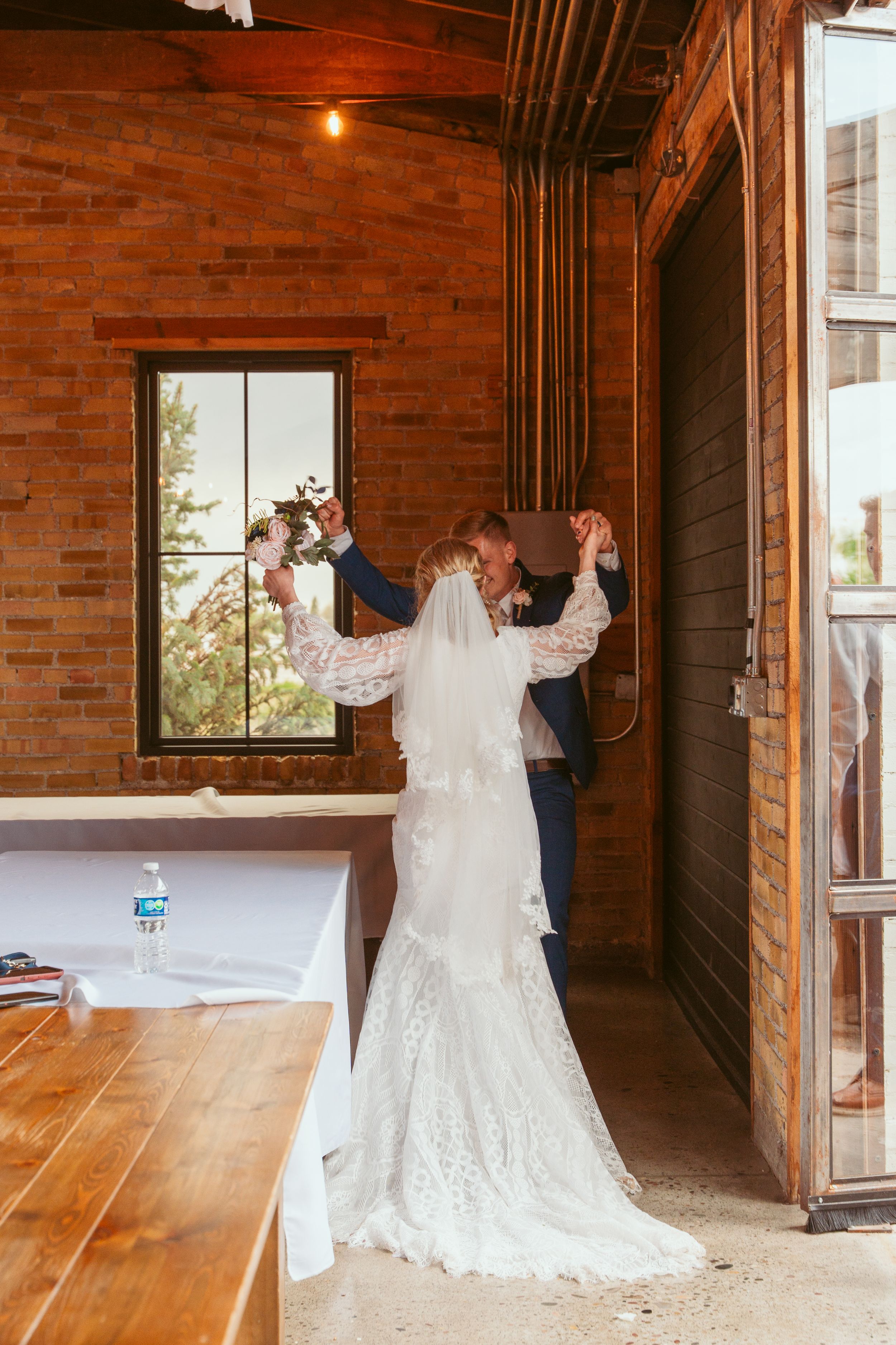 Couple dances in an industrial-style brick venue with hardwood floors and natural lighting.