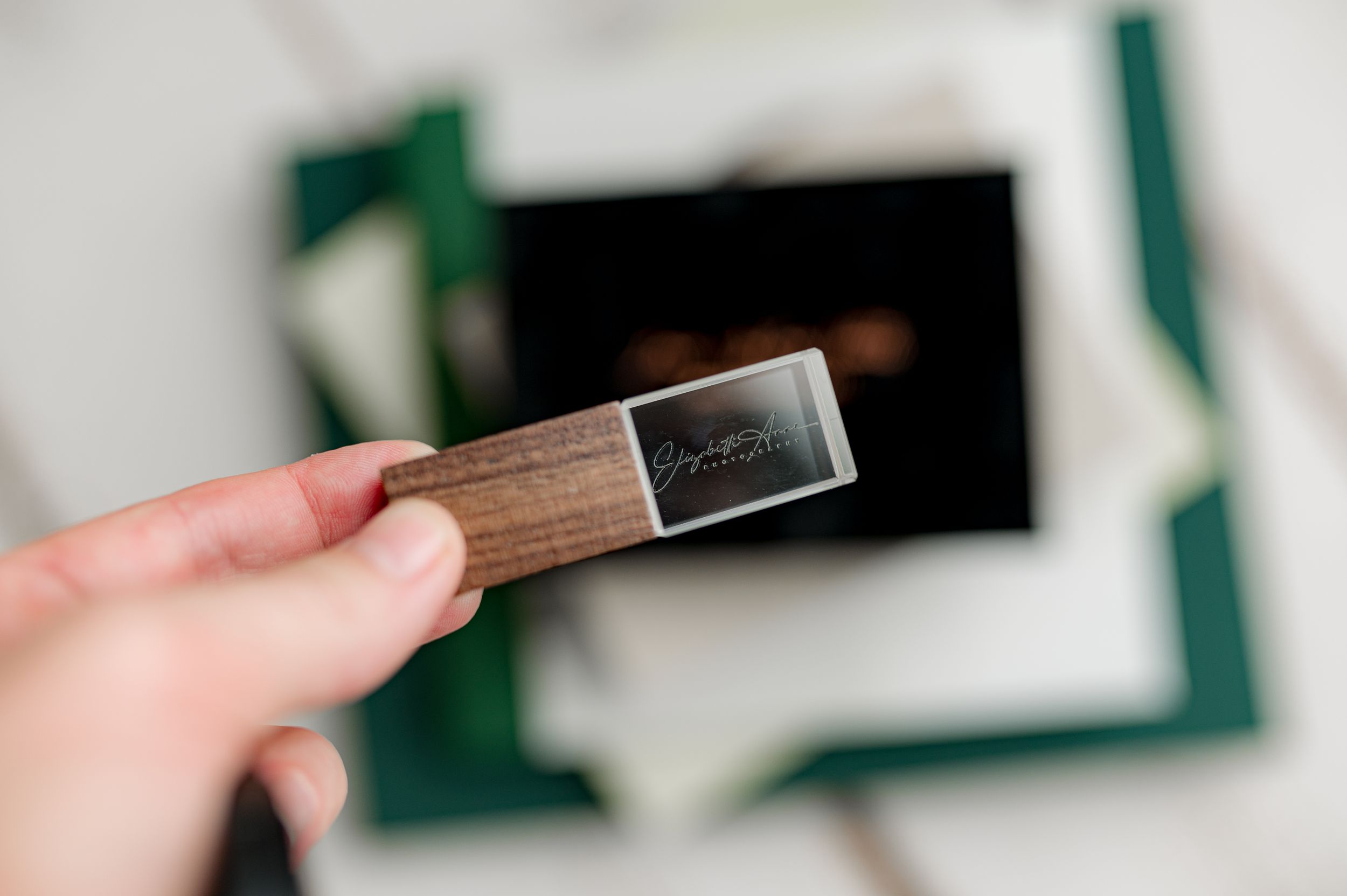 Hand holding a wooden USB drive against a background of photo packaging.