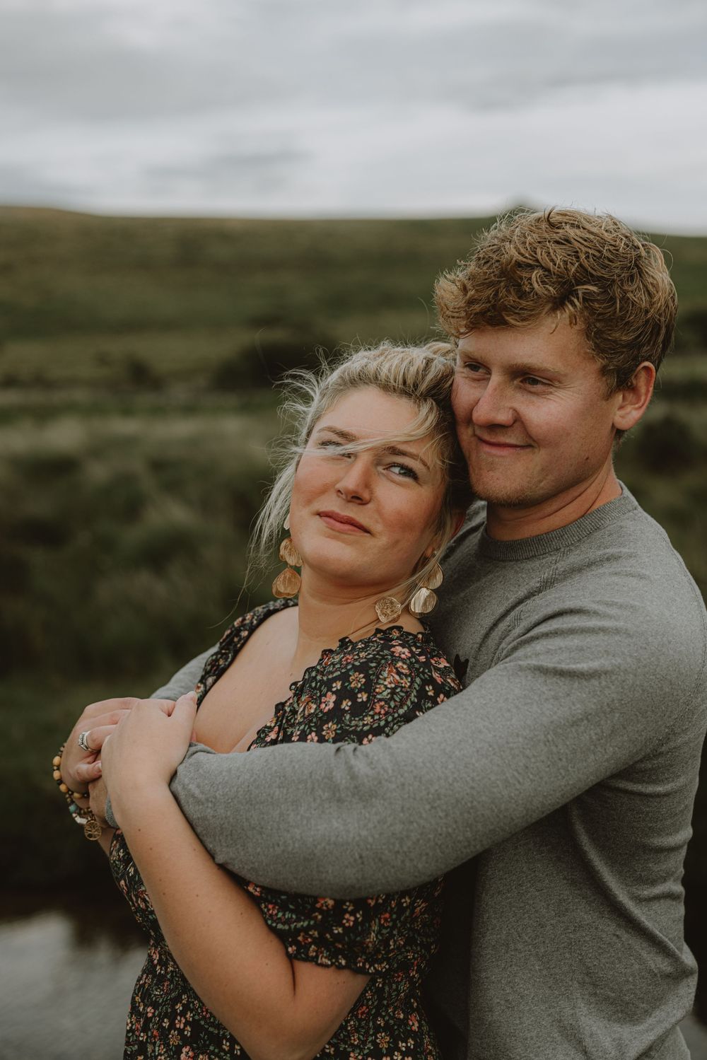 A couple embraces while standing in moody Scottish highlands landscape.