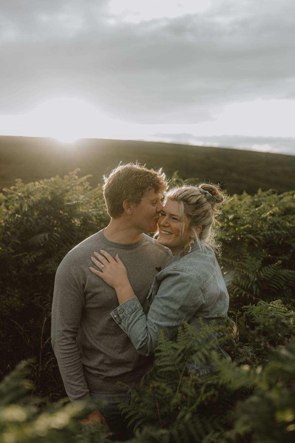 An intimate moment between a couple against a backdrop of rolling hills at sunset.