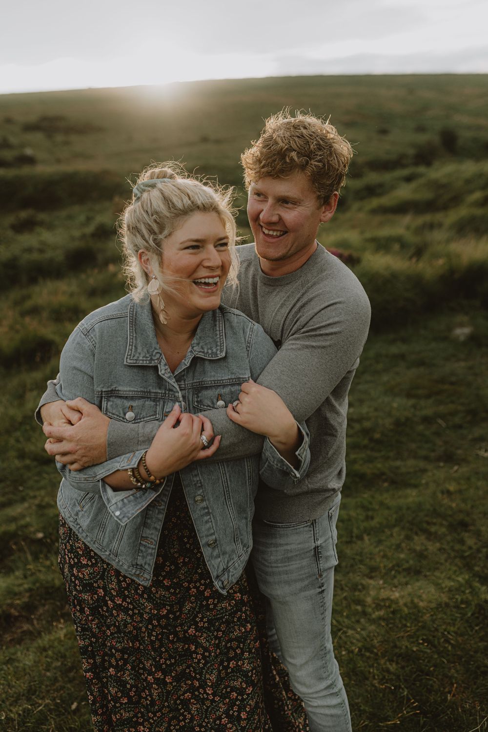 A joyful couple shares a laugh while embracing in an outdoor setting with golden light.