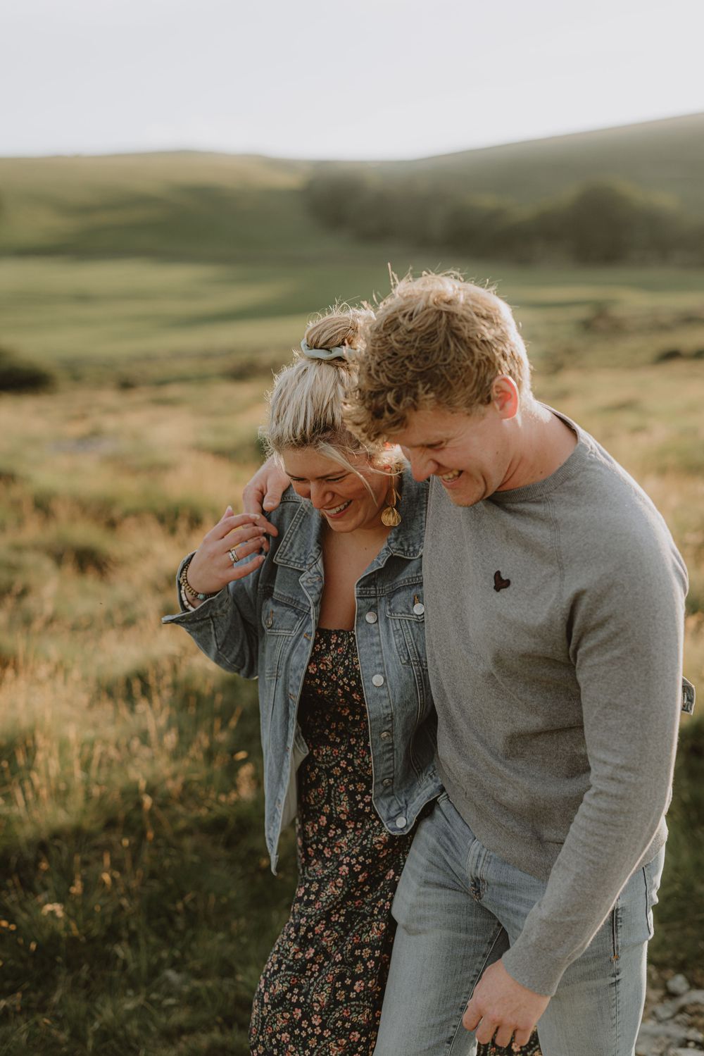 A couple shares an intimate moment while walking through tall grass on a hillside.
