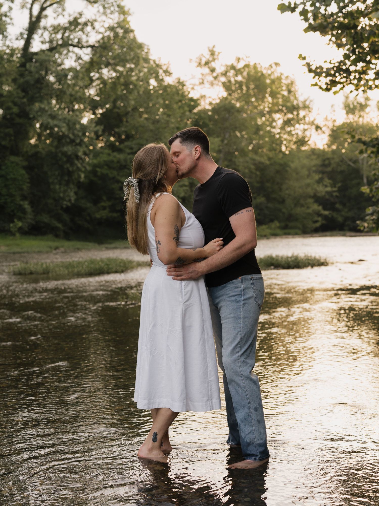 A couple sharing a joyful moment together outdoors, embracing while sitting on grass with trees in the background.