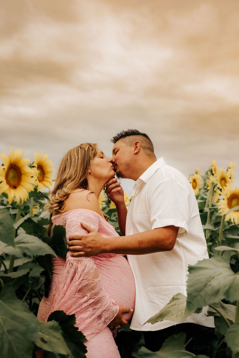 Romantic couple sharing a tender moment in a vibrant sunflower field at sunset.