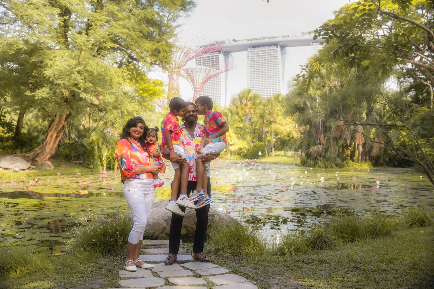 A loving family spending time together on a walkway near a tranquil pond surrounded by lush greenery on a sunny day.