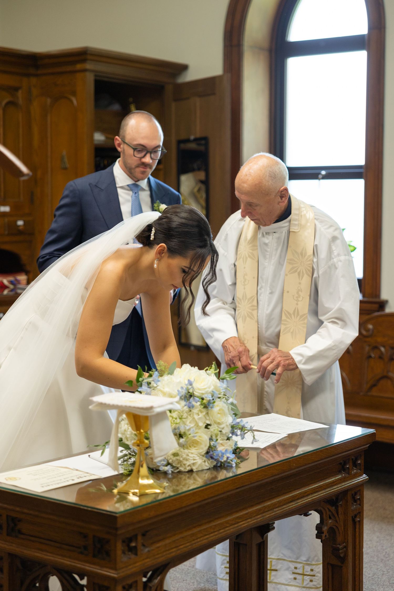 The signing of a marriage register at a traditional church ceremony with a priest and witness present. Rachel Martinez Photography