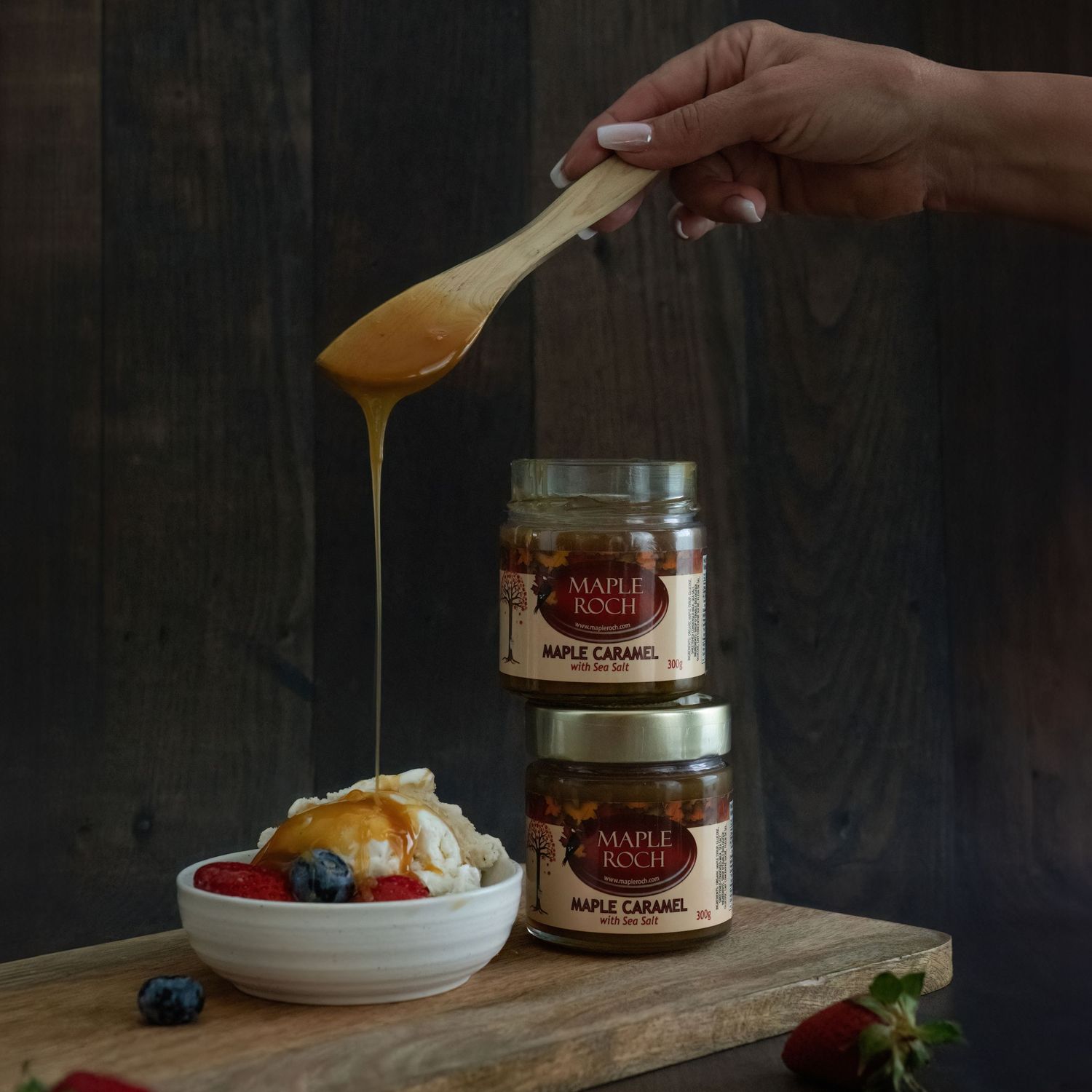 Hand drizzling Maple Roch maple caramel over vanilla ice cream  with berries beside two jars - Okanagan product photography by Tania Veitch.